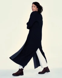 Christy Turlington wearing a long dark coat and white trousers against a pale background