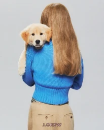 Woman with long blonde hair wearing a bright blue rollneck sweater holding a golden puppy against a grey seamless background