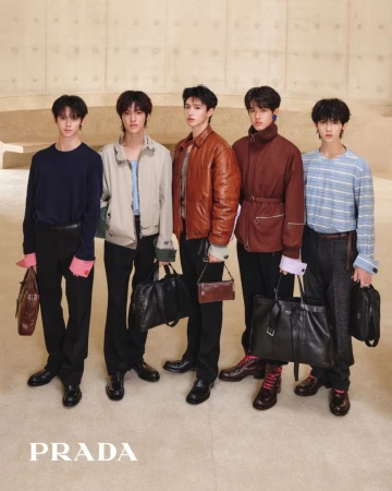 Five young East Asian men posing in Prada menswear and holding designer leather bags against a neutral beige concrete wall.