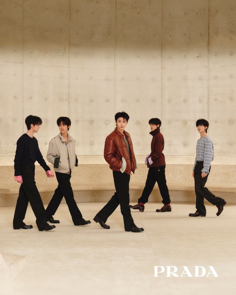 Five male models walking in Prada menswear against a smooth architectural concrete wall.