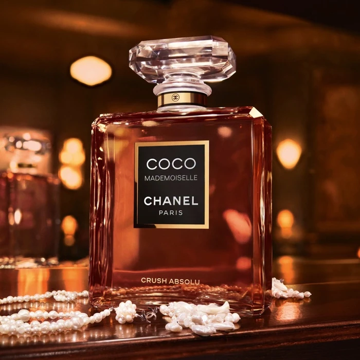 Chanel Coco Mademoiselle Crush Absolu perfume bottle resting on a dark wooden surface with scattered pearls