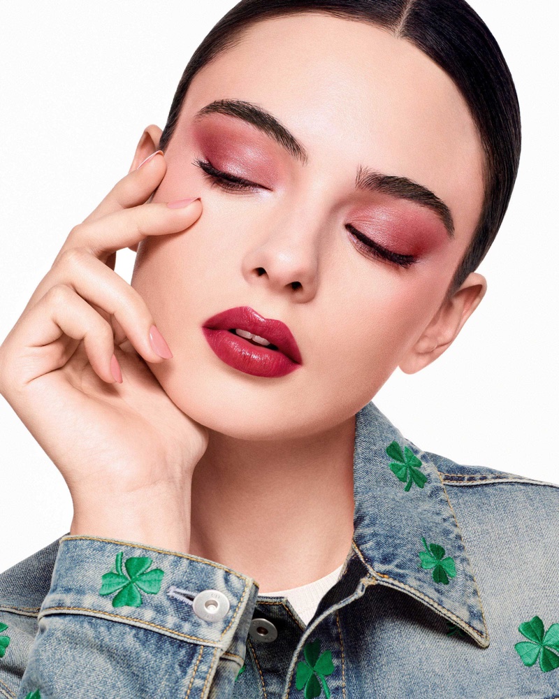 Deva Cassel in Dior beauty campaign wearing pink eyeshadow and denim jacket with green embroidered clovers against a white background