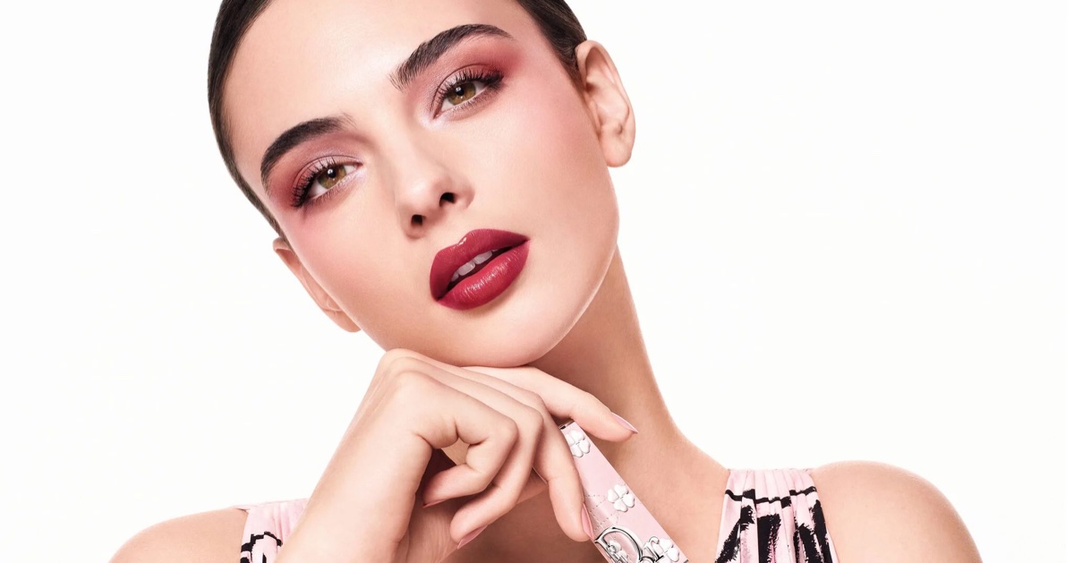 Deva Cassel in a Dior beauty campaign wearing pink eyeshadow and dark lipstick holding a patterned makeup product against a white background.