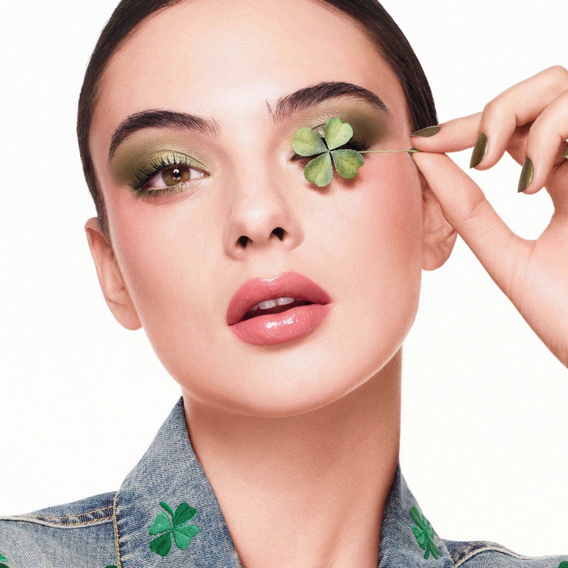 Close-up portrait of model Deva Cassel holding a four-leaf clover over her eye for the Dior Lucky Clover campaign