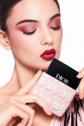 Model Deva Cassel holding a pink quilted Dior cosmetics case with clover appliqués in a beauty campaign