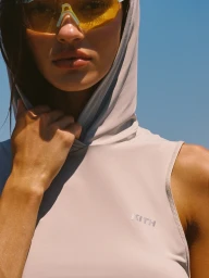 Model wearing yellow sunglasses and a hooded grey top against a bright blue sky for Kith Between Tides project