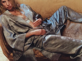 Charlotte McKinney reclining on a vintage upholstered sofa wearing a patterned grey silk robe and matching trousers for NakedCashmere Boudoir