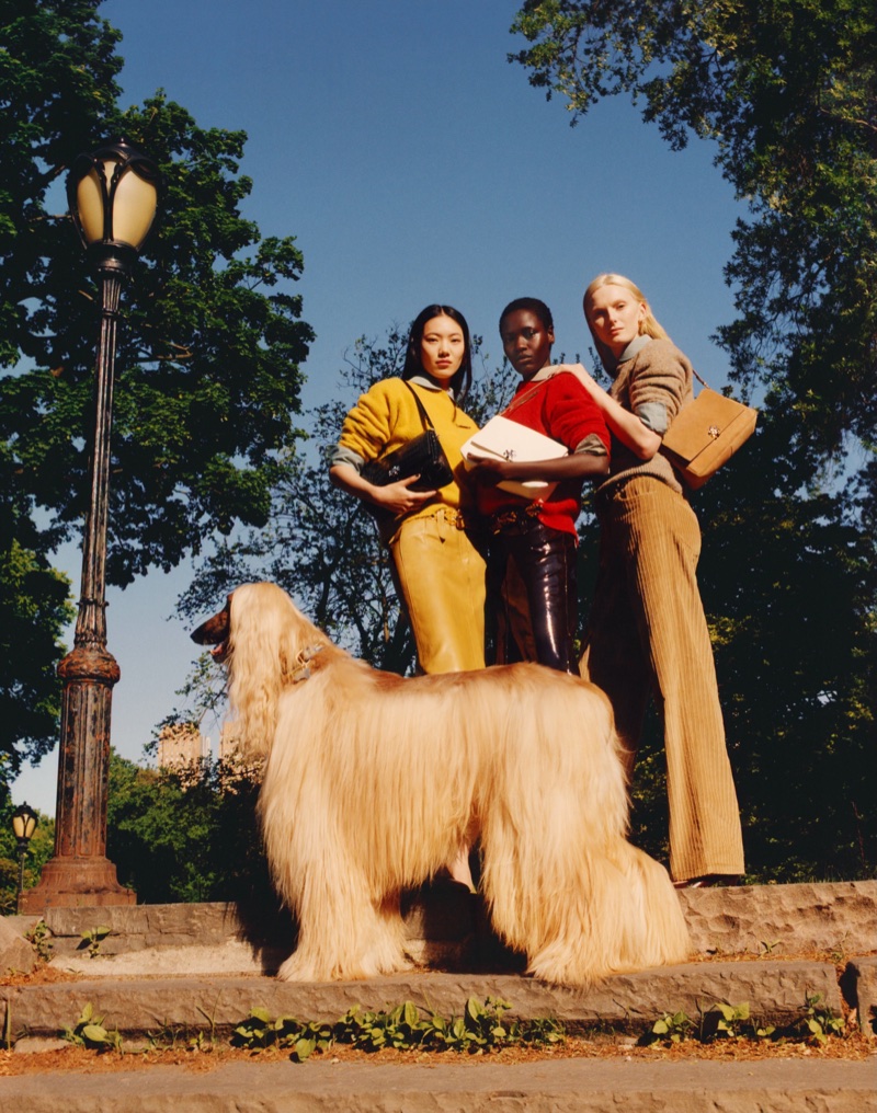 Alex Consani, Awar Odhiang, and Hejia Lee posing with an Afghan hound and handbags on park steps for Tory Burch.
