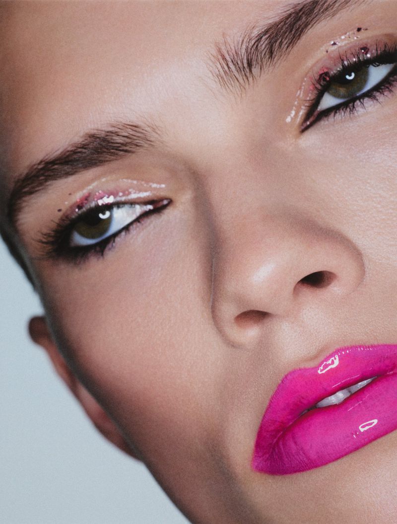 Extreme close-up beauty portrait of a model with glossy hot pink lips, winged eyeliner, and glossy eyeshadow.