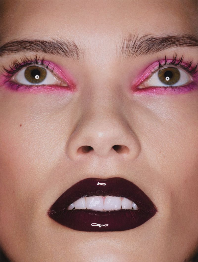 Extreme close-up beauty shot of a woman with bright pink eye makeup and glossy dark burgundy lipstick.