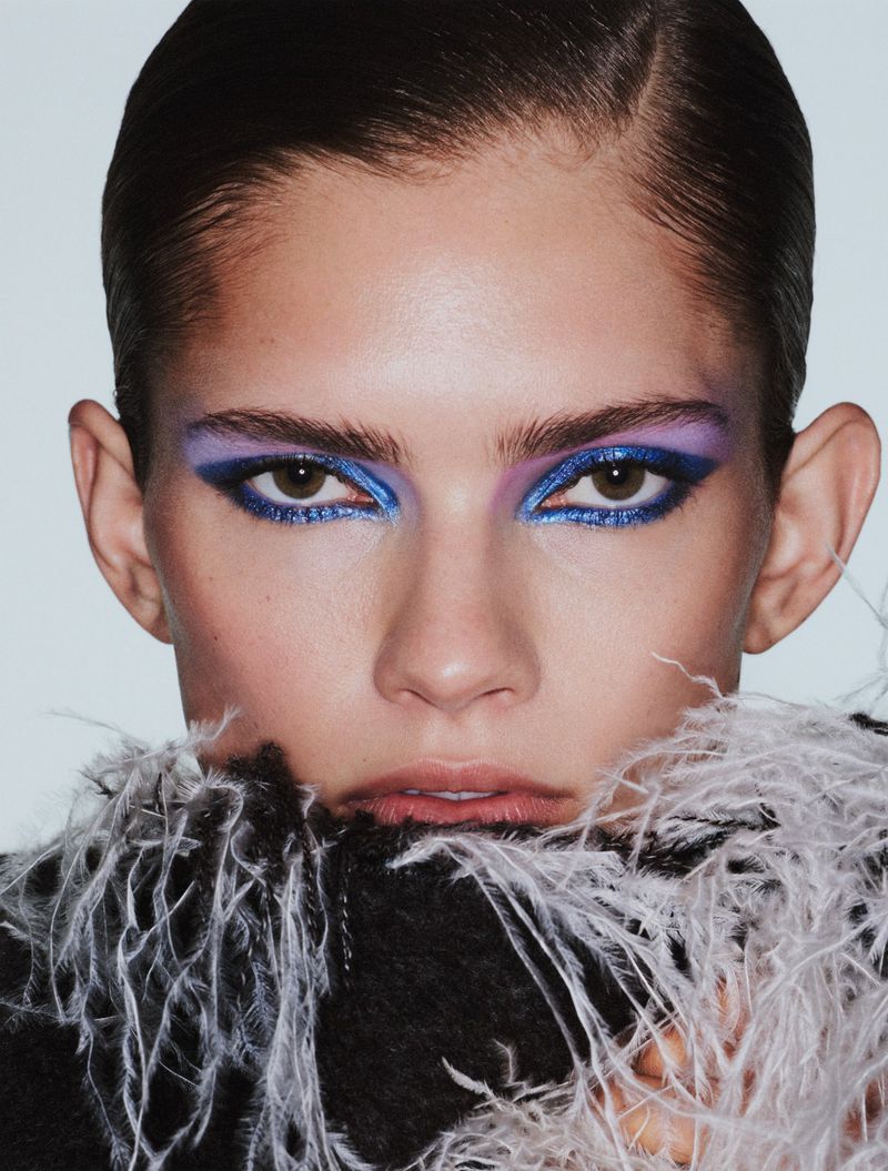 Close-up beauty portrait of model Wilda Rubin with bold blue graphic eyeliner, purple eyeshadow, and a white feather collar.