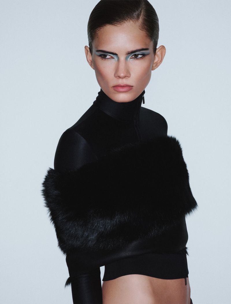 Model Wilda Rubin wearing a black fur-trimmed top with graphic blue eye makeup against a pale studio background.