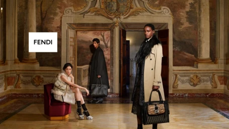 Three models pose in an opulent ornate hotel lobby holding Fendi handbags and wearing designer autumn coats.