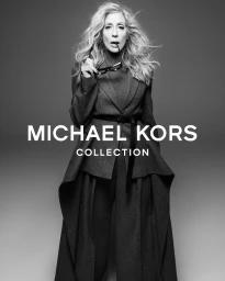Judith Light in a belted grey coat holding glasses against a seamless backdrop
