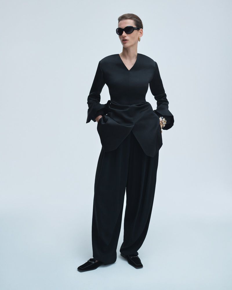 Model Giedre Dukauskaite posing in an all-black tailored ensemble with sunglasses against a seamless studio backdrop.