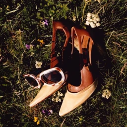 Brown leather high heels and tortoiseshell sunglasses resting on lush green grass