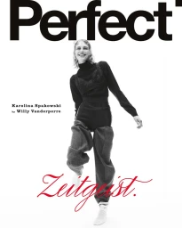 Model Karolina Spakowski posing dynamically in a black top and grey trousers on a white studio background.