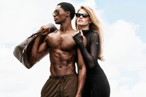 Man holding a duffel bag and woman wearing sunglasses against a cloudy sky