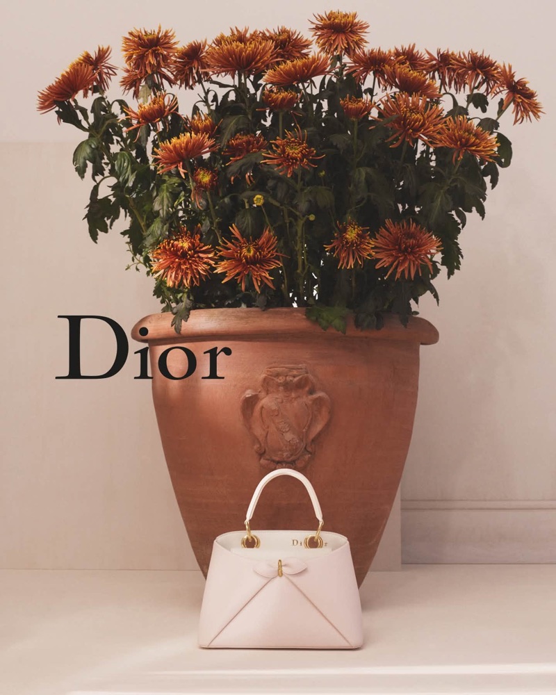 Dior white leather handbag placed in front of a terracotta planter filled with rust-coloured flowers against a neutral wall.