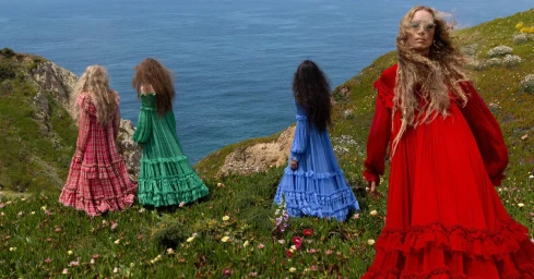Four models in long colorful ruffled dresses standing on a coastal cliff above the ocean for Chloe Fall-Winter 2026 campaign.