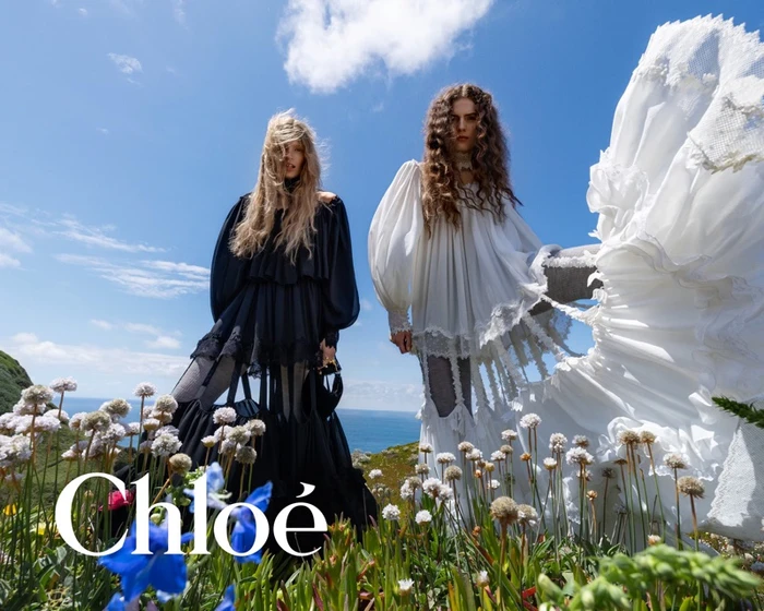Two female models standing in a wildflower field against a bright blue sky for the Chloé Fall-Winter 2026 campaign.