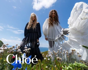 Two female models standing in a wildflower field against a bright blue sky for the Chloé Fall-Winter 2026 campaign.