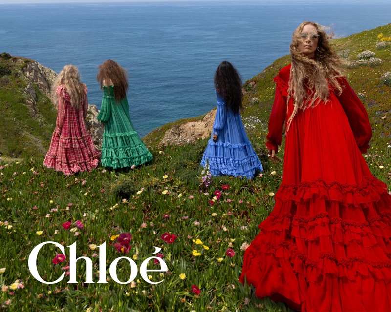 Four women in colorful ruffled dresses standing on a coastal cliff above the ocean in the Chloé Fall-Winter 2026 campaign.