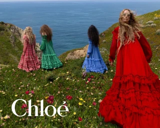 Four women in colorful ruffled dresses standing on a coastal cliff above the ocean in the Chloé Fall-Winter 2026 campaign.