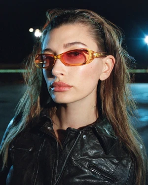 Hailey Bieber wearing amber-tinted sunglasses and a black leather jacket outdoors at night for Miu Miu