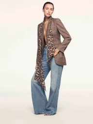 Model Irina Shayk wearing a brown plaid blazer with a leopard print scarf and blue jeans against a light background