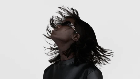 Model wearing dark sunglasses with hair blowing in the wind against a plain light background for Balenciaga Gossip project