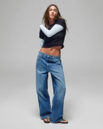 Hailey Bieber wearing layered tops and low-rise blue denim jeans against a plain grey background