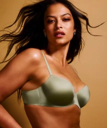 Model wearing a sage green balconette bra against a warm golden background with hair blowing in the wind.