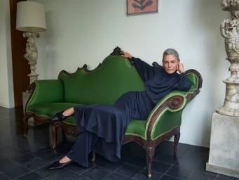 Woman in dark clothing lounging on an ornate green velvet sofa in a brightly lit interior space