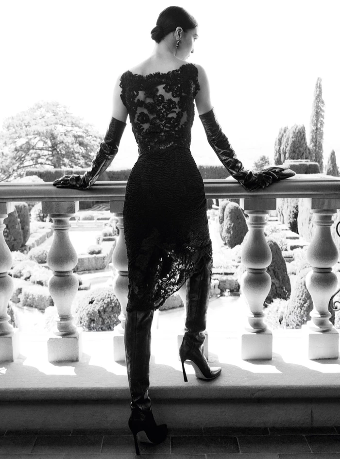 Model in black lace dress and high leather boots standing on a terrace overlooking gardens for Ermanno Scervino Fall-Winter 2026
