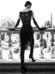 Model in black lace dress and high leather boots standing on a terrace overlooking gardens for Ermanno Scervino Fall-Winter 2026