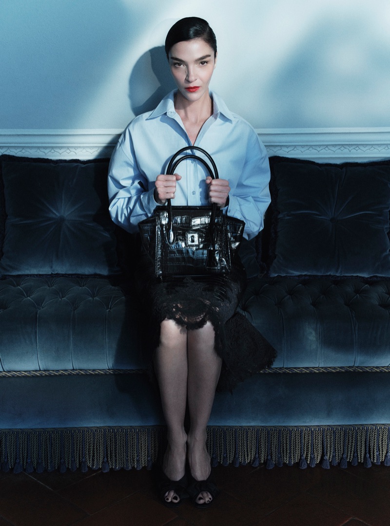 Mariacarla Boscono seated on a dark tufted sofa holding a black leather handbag for Ermanno Scervino Fall-Winter 2026 campaign