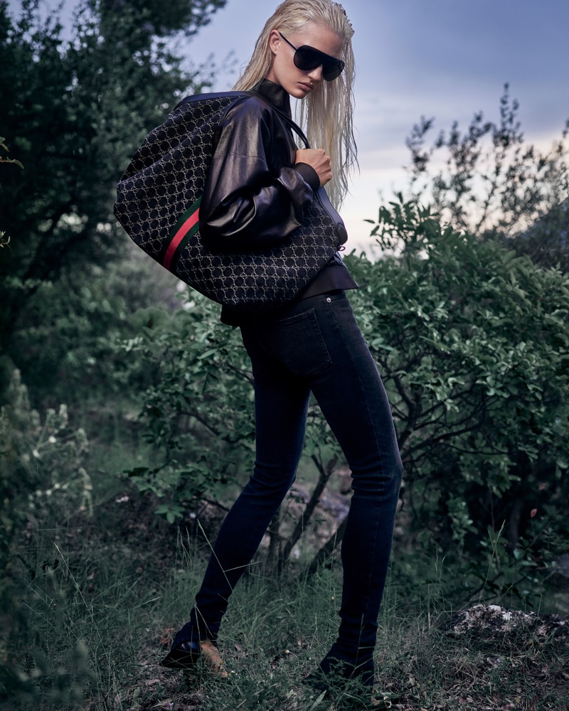 Model with wet blonde hair and large sunglasses carrying a patterned Gucci tote bag in an outdoor setting