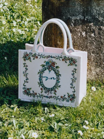 White canvas Dior tote bag with floral embroidery resting on green grass outdoors