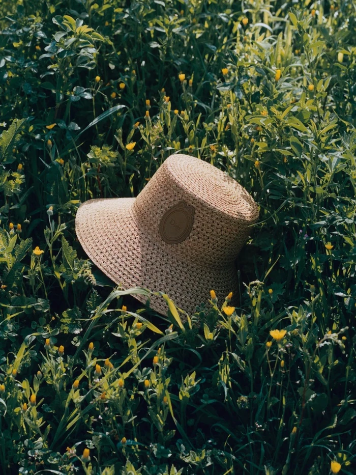 Woven straw bucket hat resting upright amidst lush green grass and small yellow wildflowers.