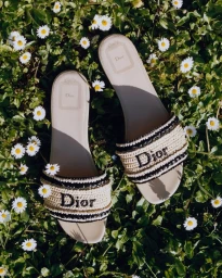 Dior slide sandals with embroidered logo resting on a patch of green grass dotted with small white daisies.