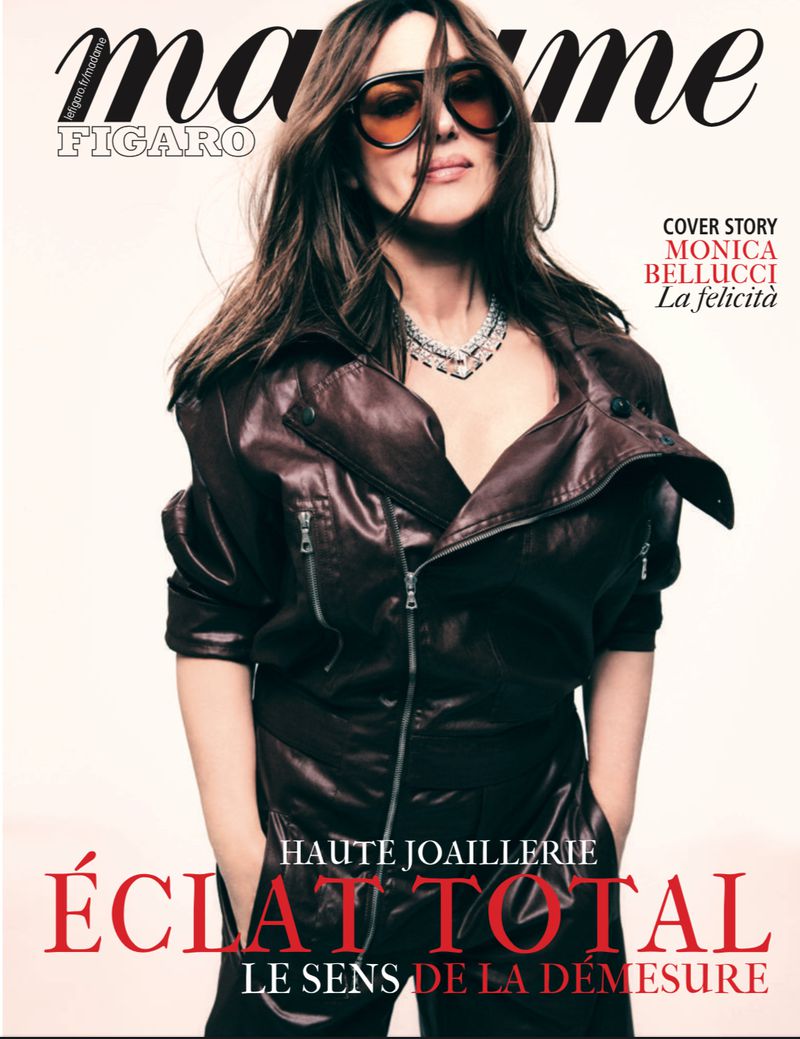Monica Bellucci graces a magazine cover in a brown leather jacket, sunglasses, and a sparkling necklace, set against a plain background.