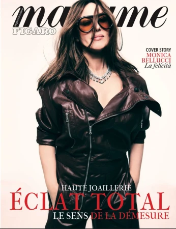 Monica Bellucci graces a magazine cover in a brown leather jacket, sunglasses, and a sparkling necklace, set against a plain background.