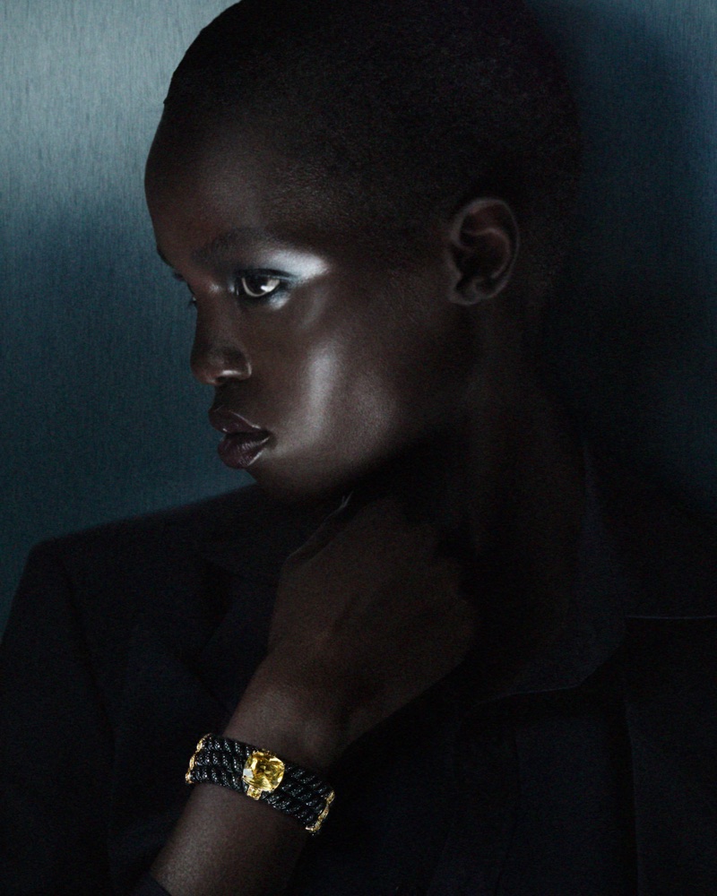 Close-up profile of a black woman wearing a black jacket and a dark braided bracelet with yellow gemstone for Gucci High Jewelry 2026.