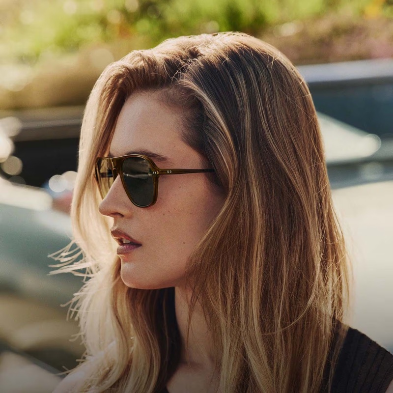 Close-up portrait of a blonde woman wearing dark sunglasses outdoors under natural sunlight.