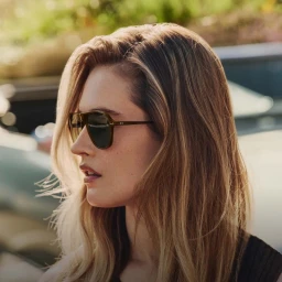 Close-up portrait of a blonde woman wearing dark sunglasses outdoors under natural sunlight.