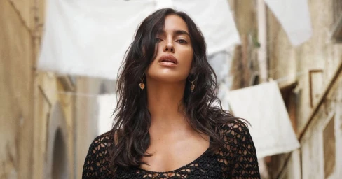 Model Irina Shayk wearing a black crocheted top with heart earrings outdoors in an alleyway for Dolce and Gabbana