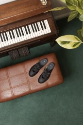 Puma Speedcat Mule shoes resting on a brown leather ottoman next to a piano and plant on a green carpet
