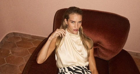 Rosie Huntington-Whiteley seated in a velvet armchair wearing a cream top and zebra print skirt