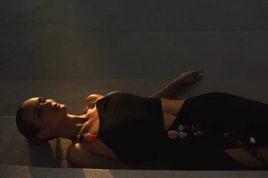 Rosie Huntington-Whiteley lying down wearing a black outfit with colourful beads on stone steps in low light